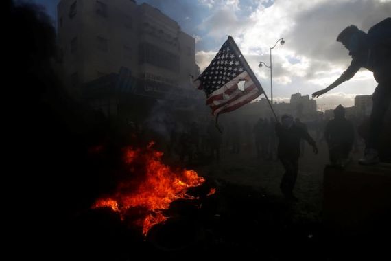 A Palestinian protester prepares to burn a U.S. flag during clashes with Israeli troops at a protest against U.S. President Donald Trump's decision to recognize Jerusalem as the capital of Israel, near the Jewish settlement of Beit El, near Ramallah